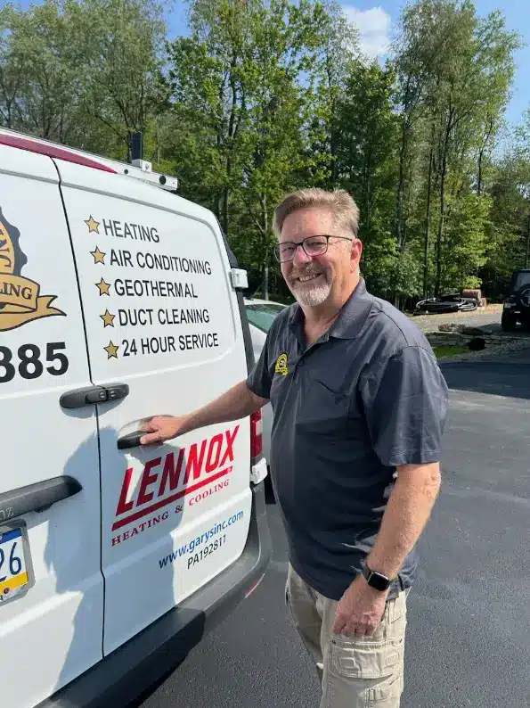 Smiling HVAC technician standing beside a service van, holding the door handle, with heating, air conditioning, and 24-hour service listed on the vehicle.